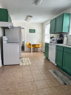 A compact kitchen with green cabinets, a white refrigerator, a microwave, and a small dining table with yellow chairs. - NEW! Residential Retreat. Located minutes to the Oceanview beach and Naval base. (Norfolk)