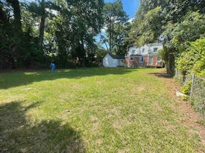 A grassy backyard with a house, a fenced area, and a person in blue clothing.