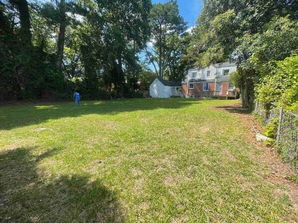 A grassy backyard with a house, a fenced area, and a person in blue clothing.