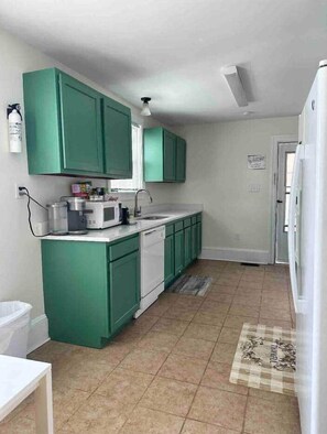 A compact kitchen with green cabinets, a white countertop, and a microwave.