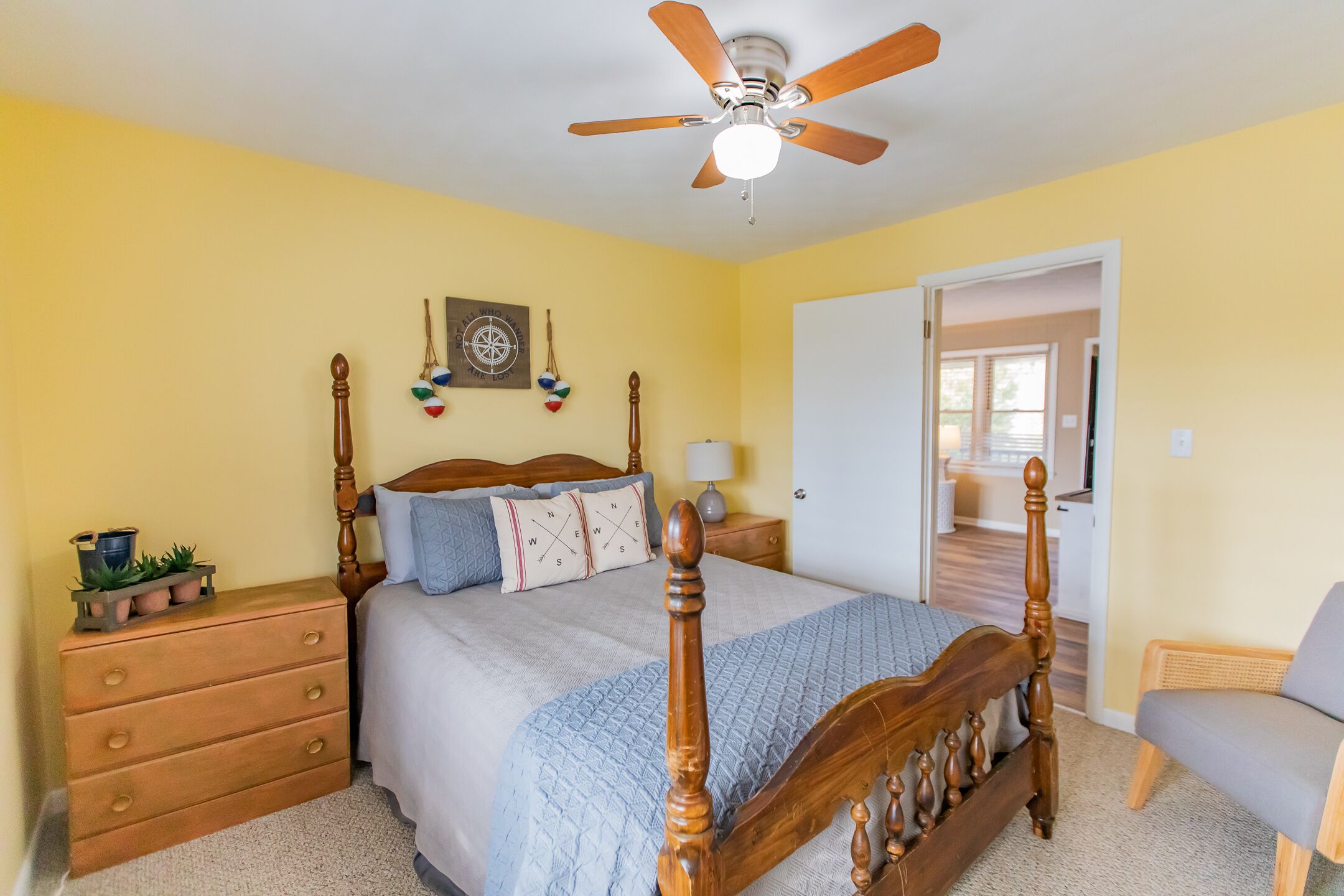 A bedroom with a wooden bed, a nightstand, a dresser, a ceiling fan, and a door leading to another room.
