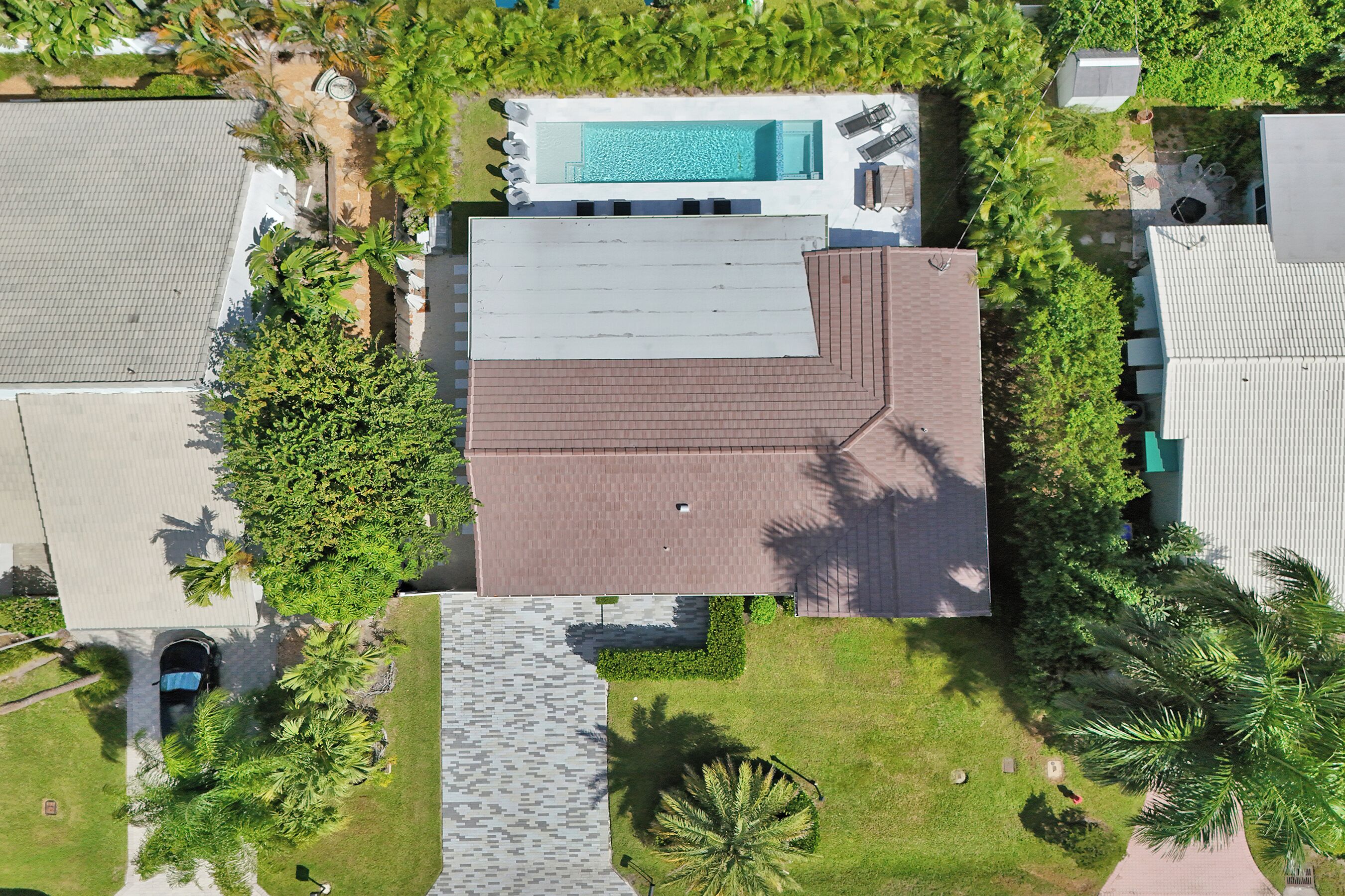 An aerial view of a house with a swimming pool, a paved patio, and surrounding greenery.