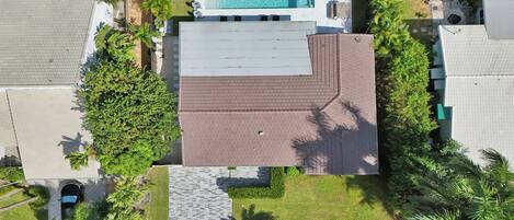 An aerial view of a house with a swimming pool, a paved patio, and surrounding greenery.