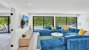 Una sala de estar moderna con un sofá seccional azul, una mesa redonda de centro y un televisor grande en la pared.