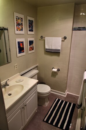 Ein Badezimmer mit Waschbecken, Toilette und Duschbereich. An der Wand hängen Bilder in Rahmen und ein Handtuchhalter mit einem Handtuch.
