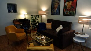 A living room with a brown sofa, yellow armchairs, a glass coffee table, and a lamp. - Lovely 1 Bedroom Garden flat in Victorian Building (San Francisco)