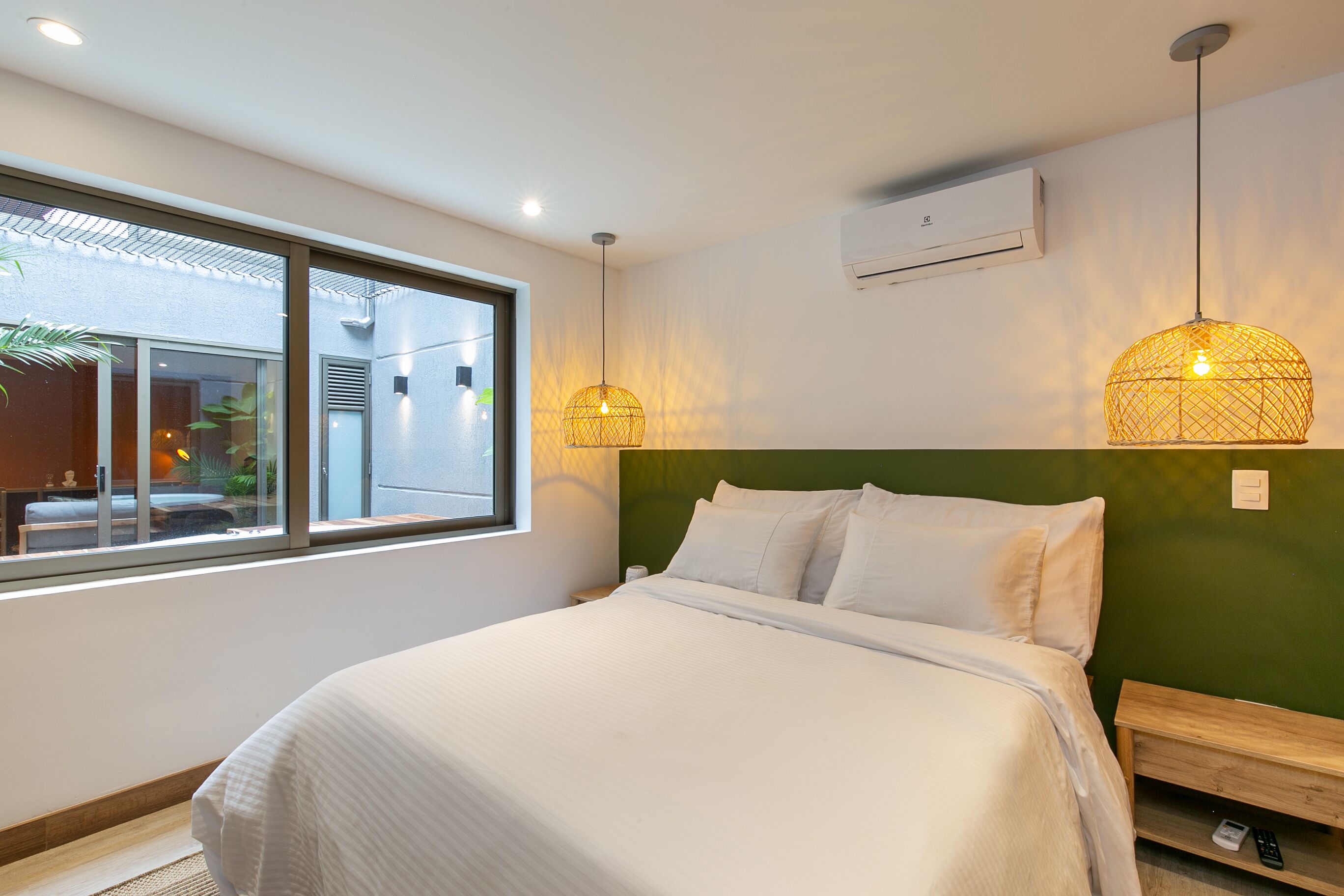 Quarto de hotel moderno com uma cama grande, duas mesas de cabeceira, uma janela com vista e duas luzes pendentes.
