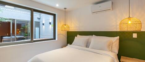 Quarto de hotel moderno com uma cama grande, duas mesas de cabeceira, uma janela com vista e duas luzes pendentes.