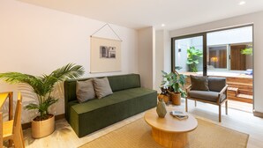 Ein modernes Wohnzimmer mit einem grünen Sofa, einem Holztisch und einem großen Fenster mit Blick ins Freie.