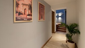 A hallway with two framed pictures on the wall, a potted plant, and a staircase leading to another room.