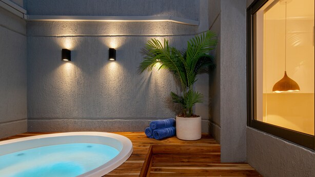 A spa area with a hot tub, wooden flooring, a potted plant, and wall-mounted lights.