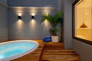 Ein Wellnessbereich mit Whirlpool, Holzboden, einer Topfpflanze und Wandleuchten.