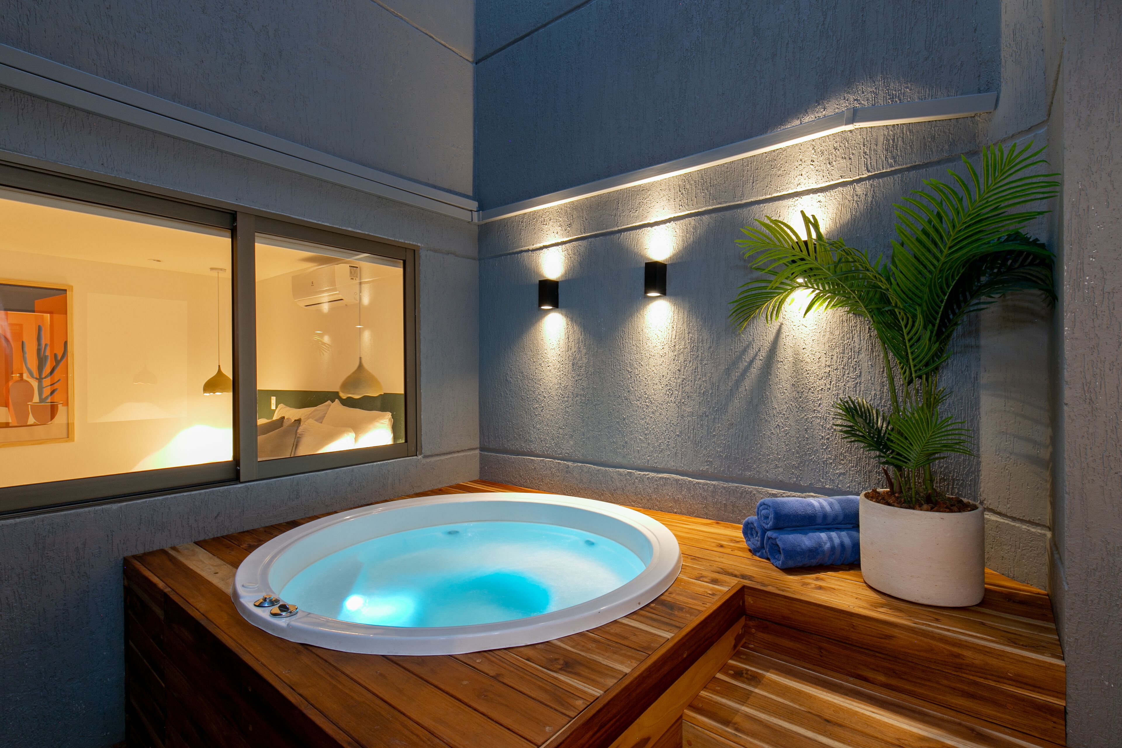 Área de spa com hidromassagem, piso de madeira, planta em vaso e uma janela com obras de arte.