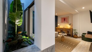 A modern interior with a large window, indoor plants, a wooden desk, and a patterned rug.