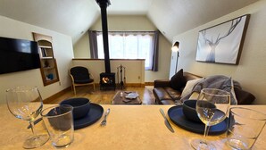 Una sala de estar acogedora con chimenea, un sofá, una mesa de comedor con copas de vino y velas, y una obra de arte enmarcada en la pared.