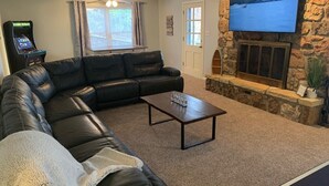 Ein Wohnzimmer mit einem schwarzen Ledersofa, einem Couchtisch, einem Kamin, einem an einer Steinwand montierten Fernseher und einer Spielkonsole.