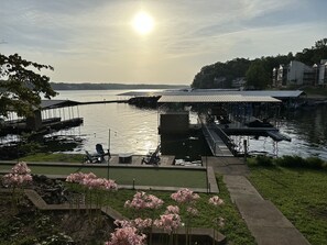A lakeside dock with a covered seating area and a grassy area with pink flowers. - Spacious Updated Lakefront House with Huge Private Dock and Bocce Ball Court (Osage Beach)
