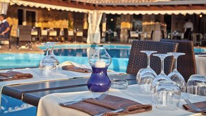 A dining table set for two with a pool view, outdoor seating, and a covered patio area. - Holiday home Two room apartment with air conditioning (Porto Rotondo)
