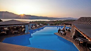 A poolside area with outdoor seating and tables, overlooking a body of water and distant mountains. - Holiday home Two room apartment with air conditioning (Porto Rotondo)