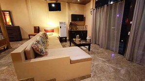A living room with a sofa, a television, a kitchen area, and a sliding door.
