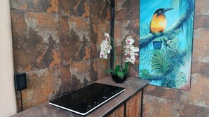 A kitchen with a black induction cooktop, a potted orchid, and a painting of a bird on a branch.