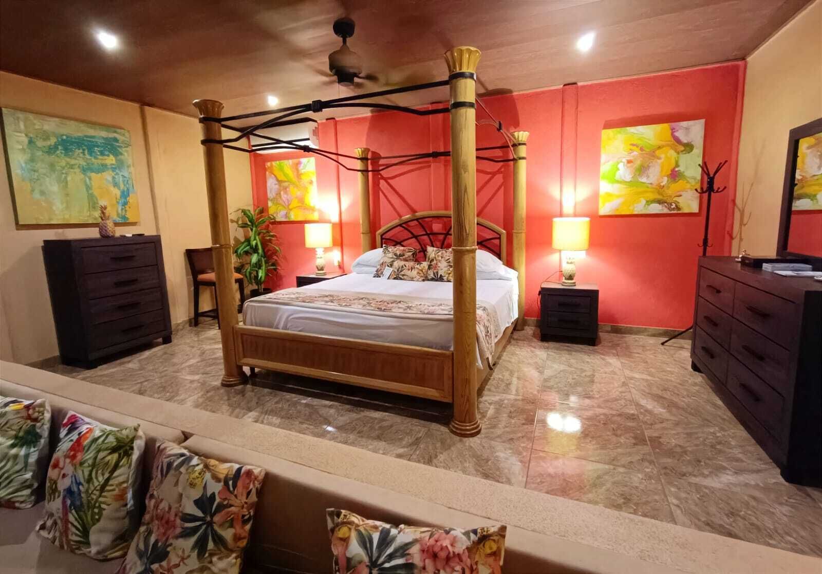 A four-poster bed with a wooden frame, a marble floor, and red walls. There are two nightstands with lamps and a dresser with a mirror.