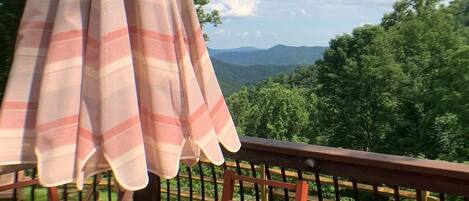 A wooden deck with a table and chairs, an umbrella, and a view of a mountainous landscape.