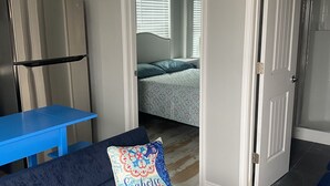 Espai vital compacte amb petita cuina, un sofà amb un coixí decoratiu, una taula blava i una porta que condueix a una altra estança.