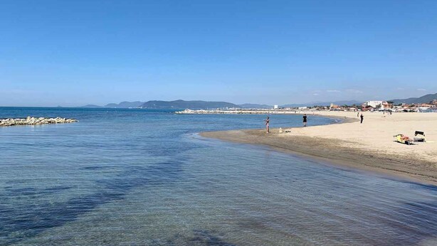 Une plage à l’eau claire, avec un rivage sablonneux et des montagnes qui se dessinent à l’horizon.