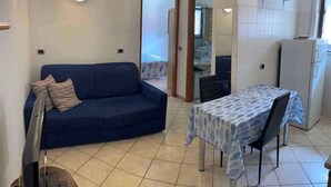 Un salon avec un canapé, une table à manger recouverte d’une nappe, un téléviseur et un coin cuisine équipé d’un réfrigérateur.