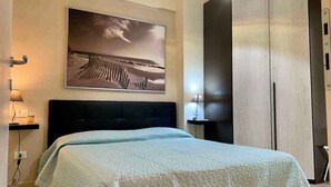 Une chambre à coucher avec un lit, une table de chevet, une lampe, une armoire et un tableau accroché au mur.