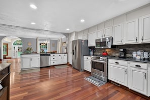 A modern kitchen with white cabinetry, stainless steel appliances, and a wooden floor.