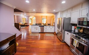 A spacious kitchen with wooden flooring, stainless steel appliances, and white cabinetry.