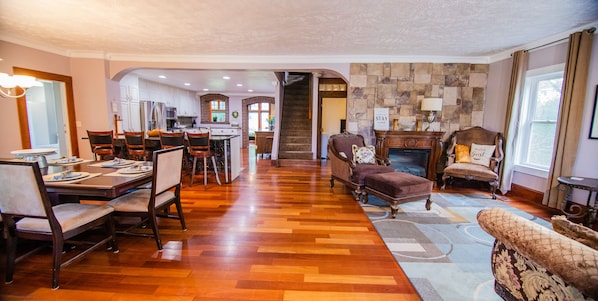 A spacious living area with a dining table set for four, a fireplace, and a view of the kitchen through an archway.