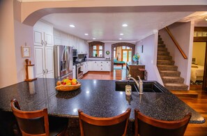 A kitchen with a large island, white cabinets, and a wooden staircase.