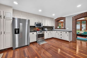 A modern kitchen with stainless steel appliances, white cabinetry, and a herringbone wood floor. - Rare find! Spacious home near wedding venues & CB/OMA. Perfect for entertaining! (Glenwood)