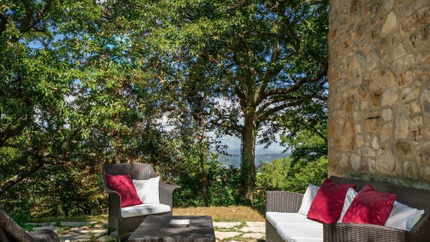 An outdoor seating area with wicker furniture and stone walls, overlooking a scenic landscape.