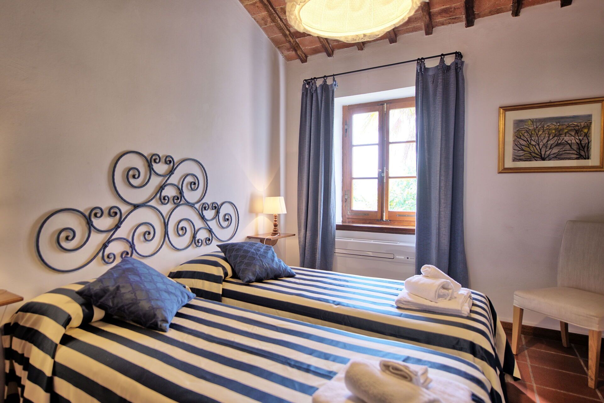 Een slaapkamer met twee bedden, een raam met gordijnen, een lamp en een stoel.