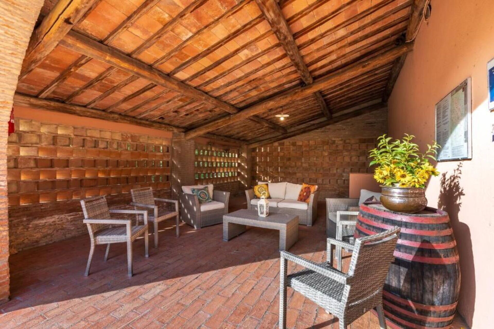 An outdoor seating area with brick walls, wooden ceiling beams, and wicker furniture.