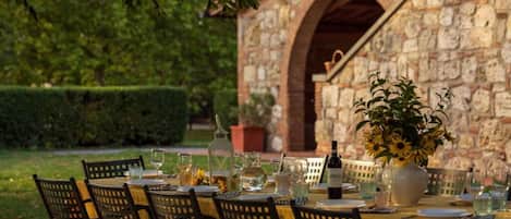 An outdoor dining area with a stone building in the background, a table set with chairs, and a vase of sunflowers.