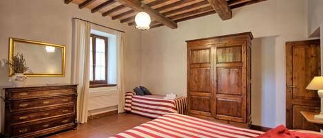 A room with two beds, a wooden wardrobe, a dresser, a mirror, and a window with curtains.