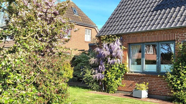 A residential house with a brick exterior, a tiled roof, and a well-maintained garden with various shrubs and flowering plants. - Hook - Holiday apartment Hook - with south-facing terrace, very quiet location (Midlum)