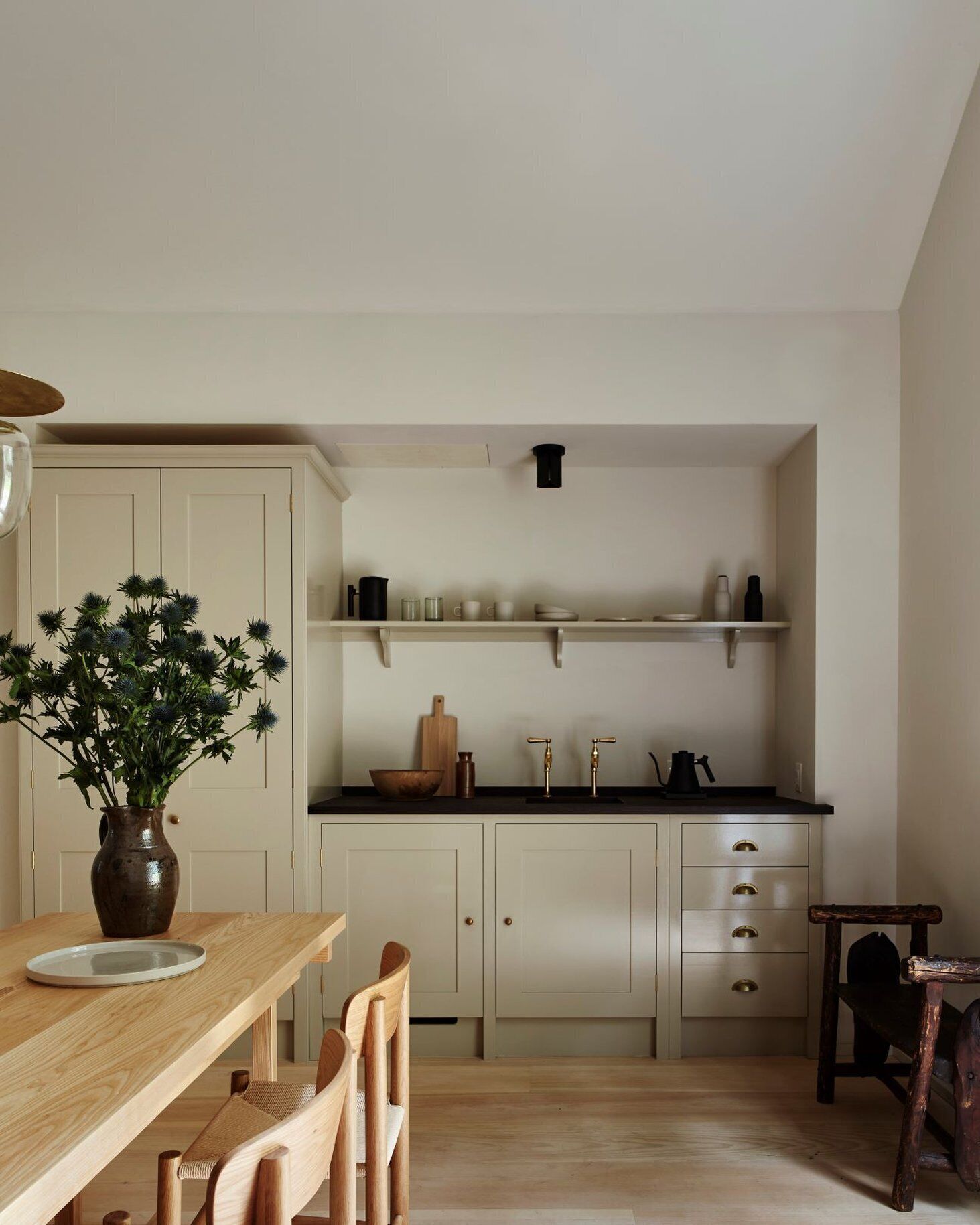 A compact kitchen with white cabinets, a wooden dining table, and a vase of flowers.