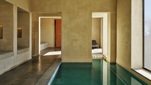 Una piscina interior moderna con diseño minimalista, destacando una superficie de agua cristalina, suelo de concreto y una paleta de colores neutros.