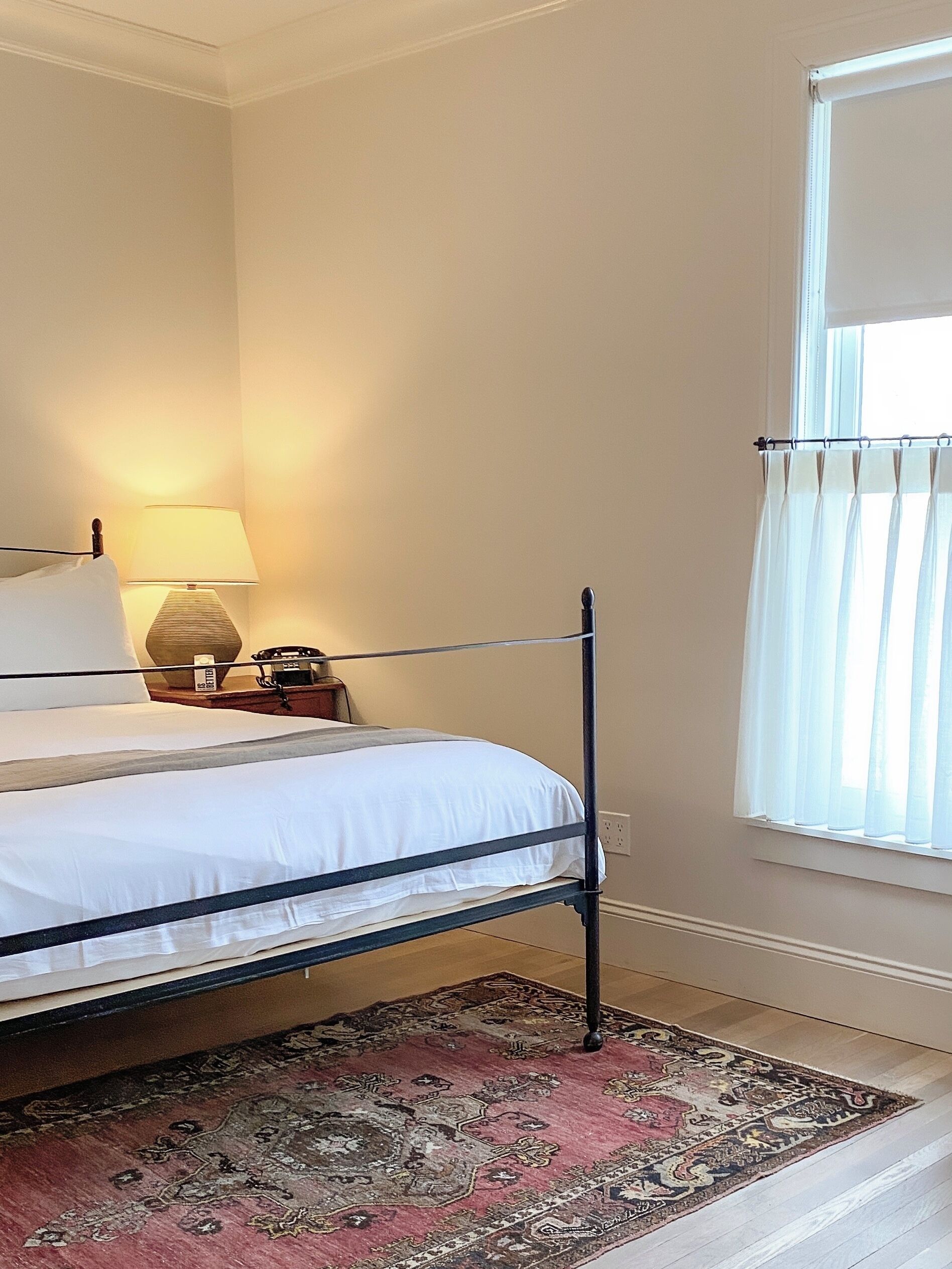 A single bed with a metal frame, a bedside lamp, a nightstand, and a patterned rug.