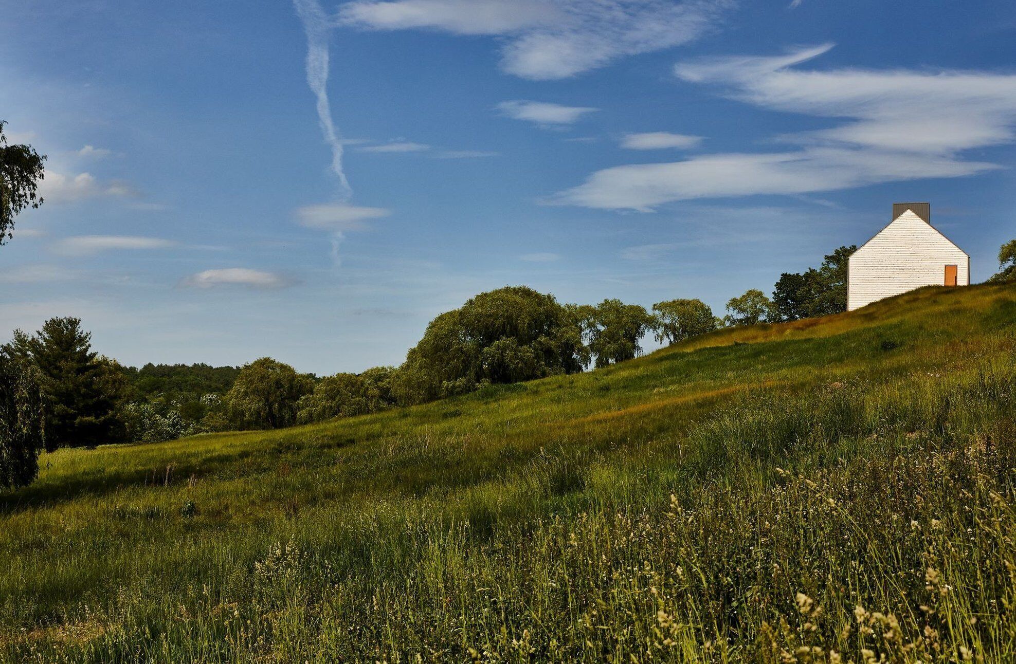 Ein weißes Gebäude mit roter Tür auf einem grasbewachsenen Hügel unter blauem Himmel.
