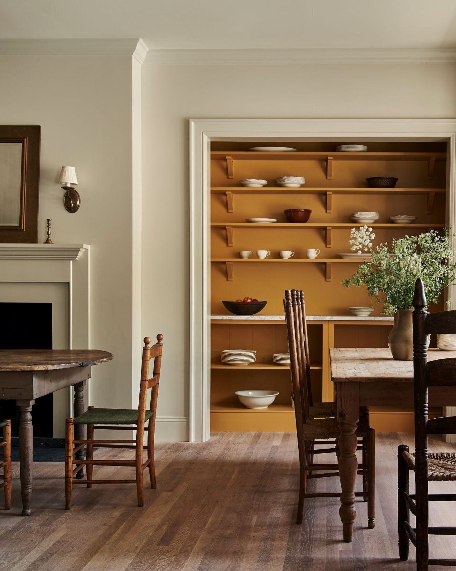Un comedor con una mesa de madera, sillas y un mueble empotrado con vajilla y un jarrón de flores.