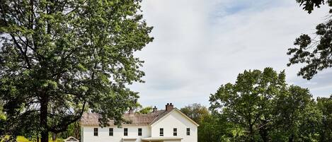 Una casa blanca de dos pisos con un porche y un árbol grande en el frente.