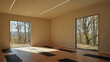 A spacious room with large windows, wooden flooring, and black mats arranged for yoga or stretching.