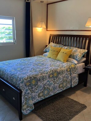 A bedroom with a bed, a nightstand, a lamp, and a window.